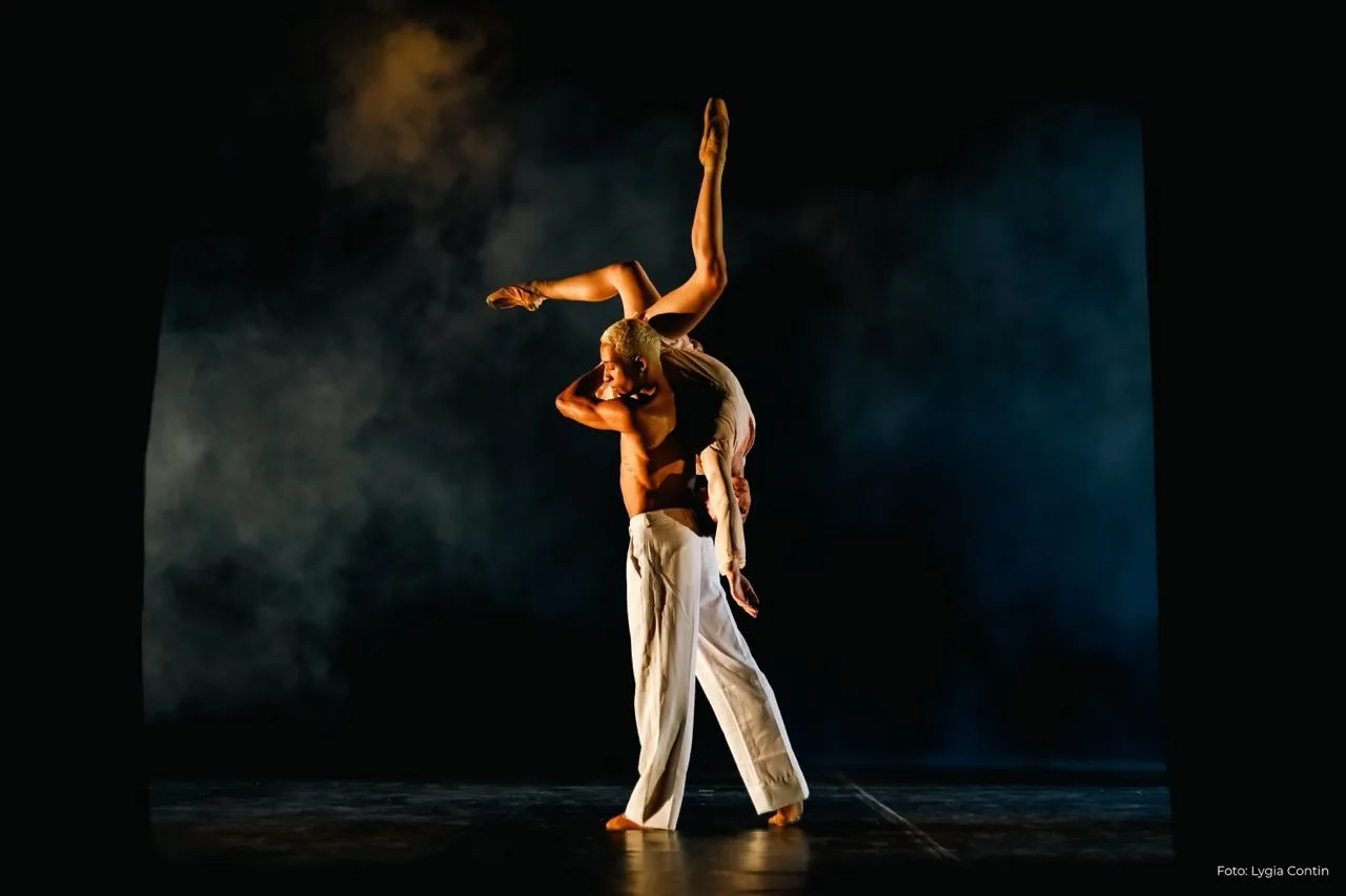 Foto do Ballet Paraisópolis na apresentação Rosto de Janus. Um corpo no meio do palco está entre "vultos" de corpos em movimento.