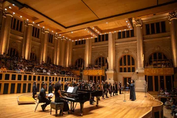 Crianças do coro infantil, vestindo preto, cantando no palco da Sala São Paulo.