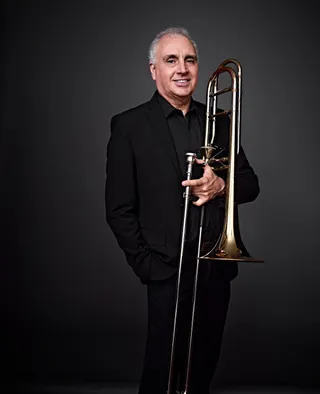 Fernando Chipoleti is a white man with white hair. He wears black and holds a trombone.