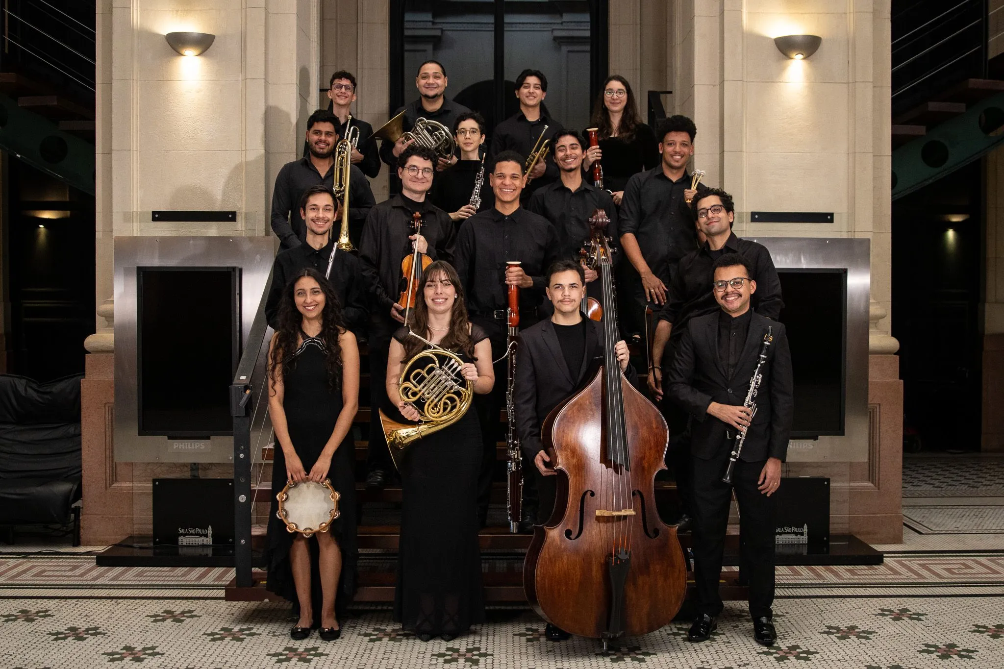 Os jovens estudantes da Academia de Música estão segurando seus instrumentos em uma escada na Sala São Paulo.