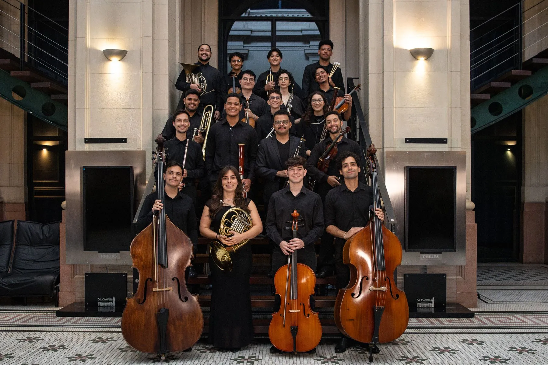 Os jovens estudantes da Academia de Música estão segurando seus instrumentos em uma escada na Sala São Paulo.