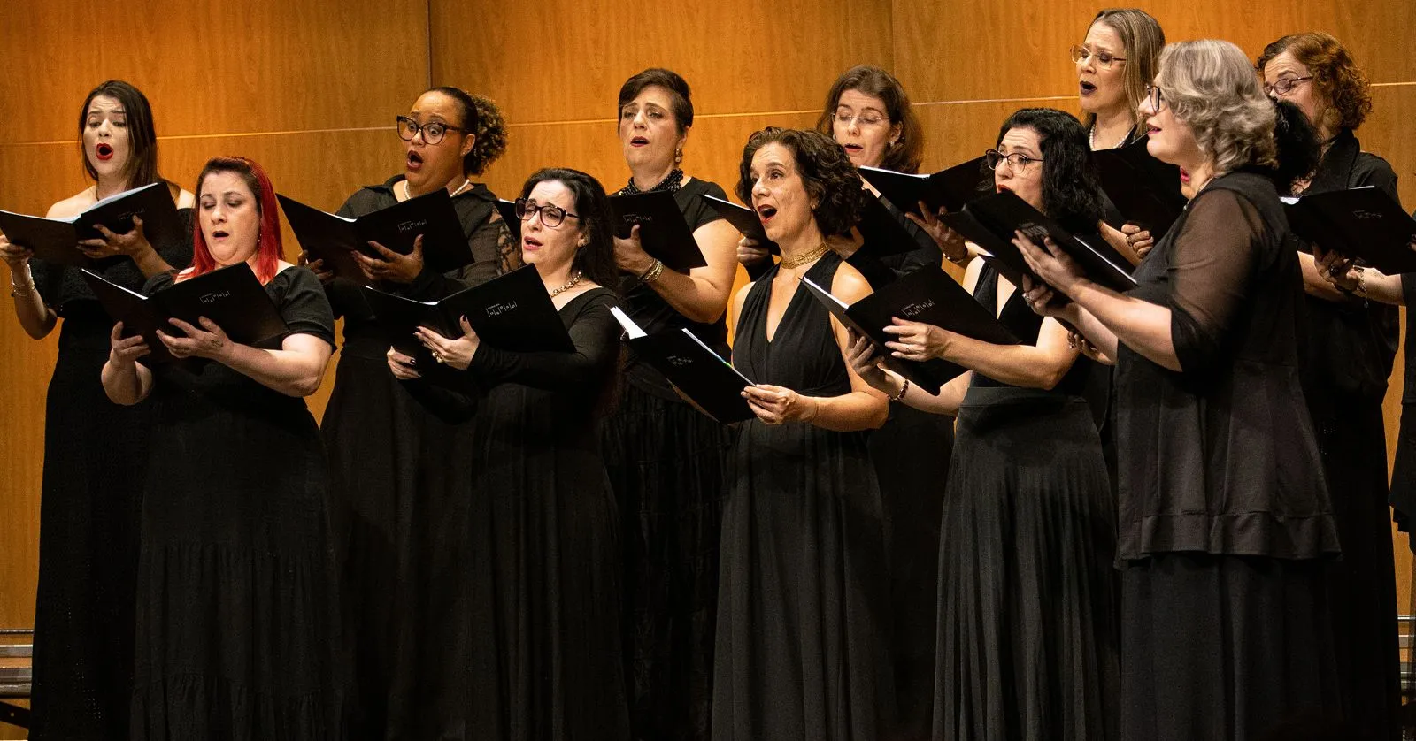 As mulheres do Coro vestem preto e cantam com as pastas na mão.