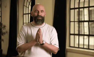 Foto de Pierre Bleuse, homem branco e careca. Ele possui barba cheia e bigode. Veste uma camiseta branca e um relógio prata no pulso esquerdo.