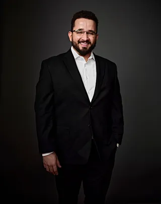 Jabez é um homem branco, na casa dos 30 anos, com cabelo castanho, barba e bigode. Ele está usando uma camisa branca e um paletó preto. Está de óculos e sorrindo na foto.