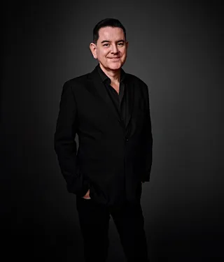 Paulo Cerqueira is a white man with short black hair. He is wearing a black shirt with the last button of the collar open. He is smiling in the photo.